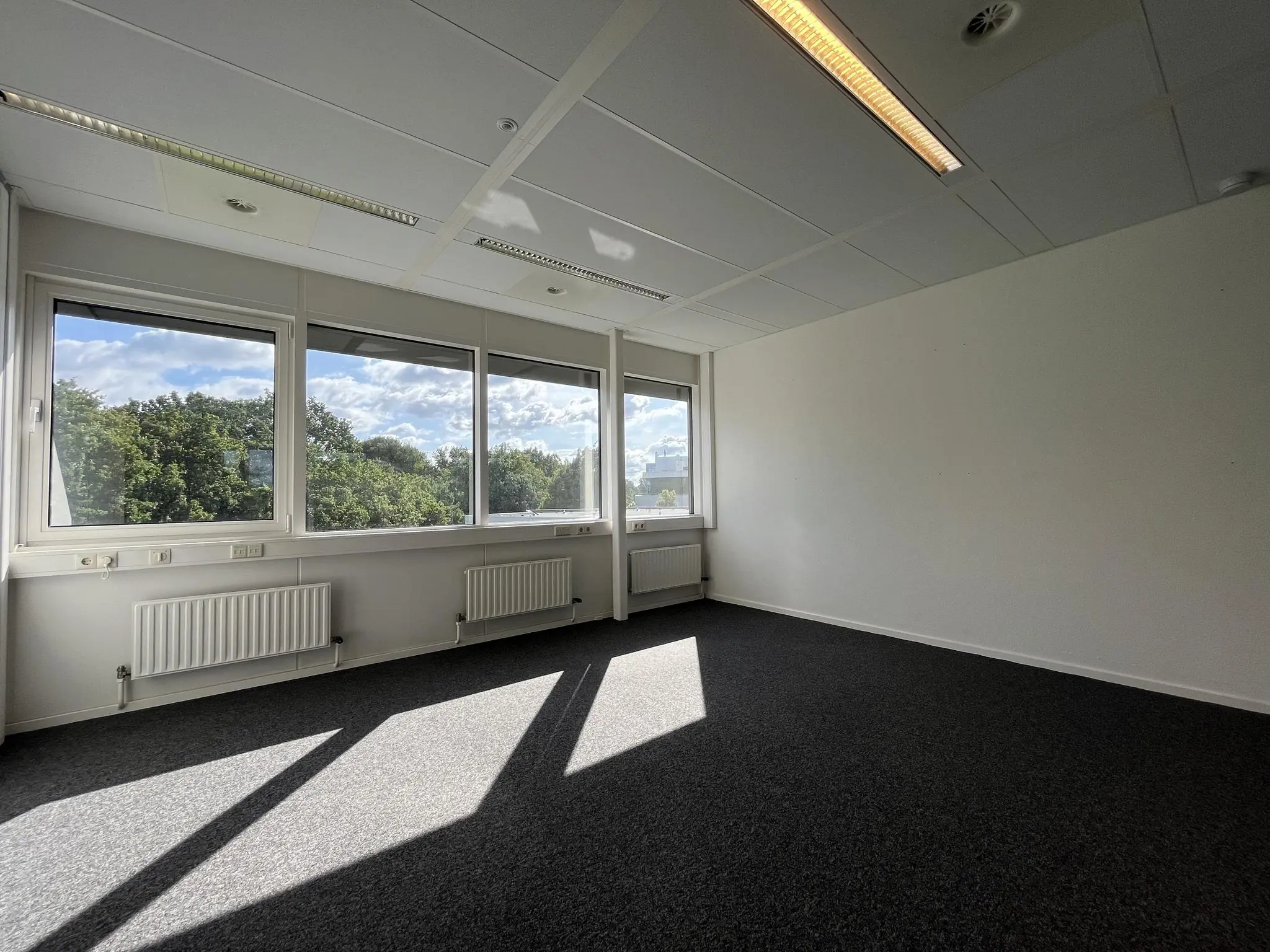 Leeg kantoor op de Baarnsche Dijk met grote ramen en uitzicht op bomen.